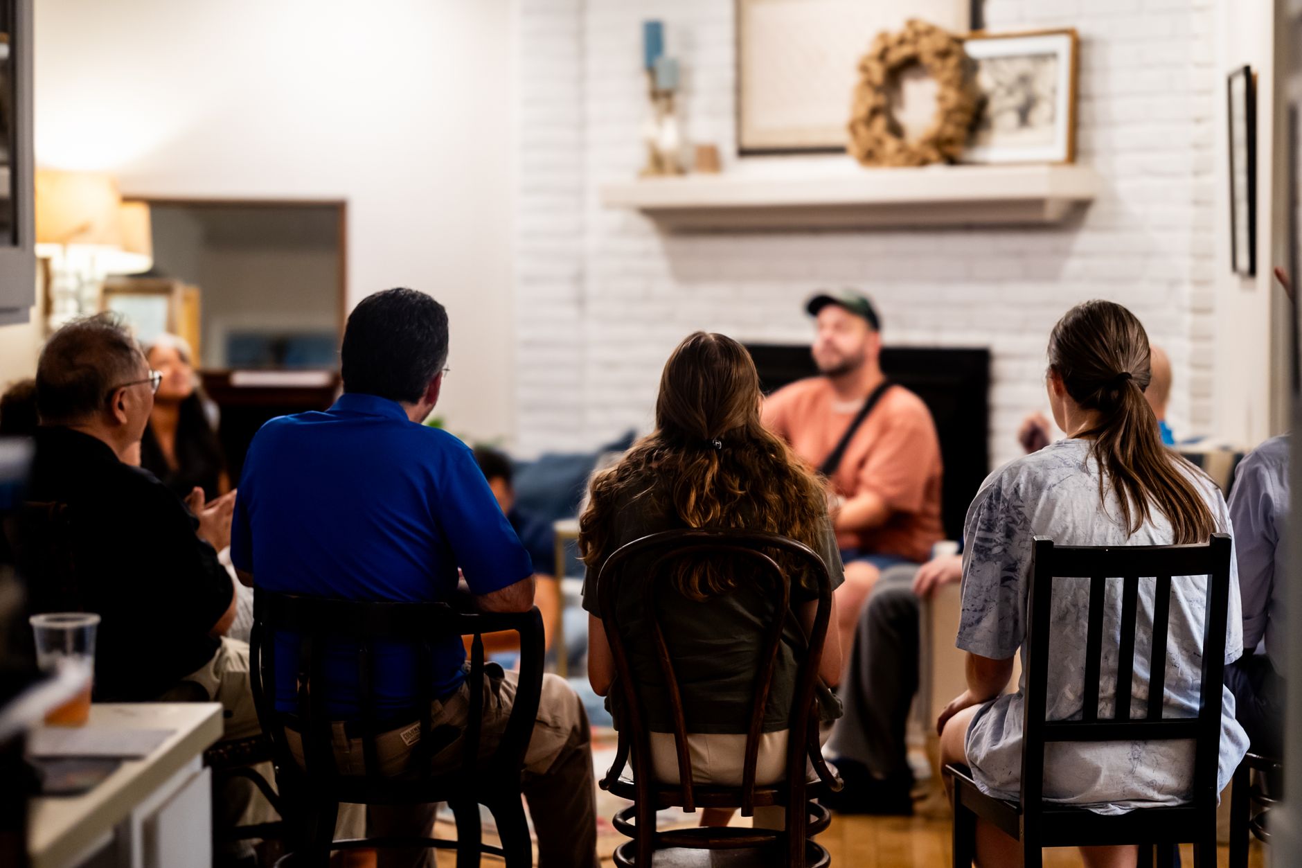 A group of people sitting in chairs, attentively listening to a musician performing in a cozy living room setting.